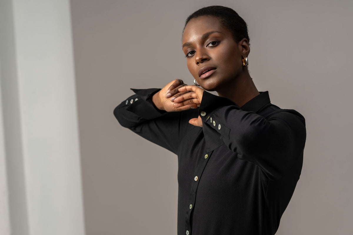 A woman wearing a long sleeve black cotton jersey shirt with a classic collar, buttoned cuffs, and a half placket front.